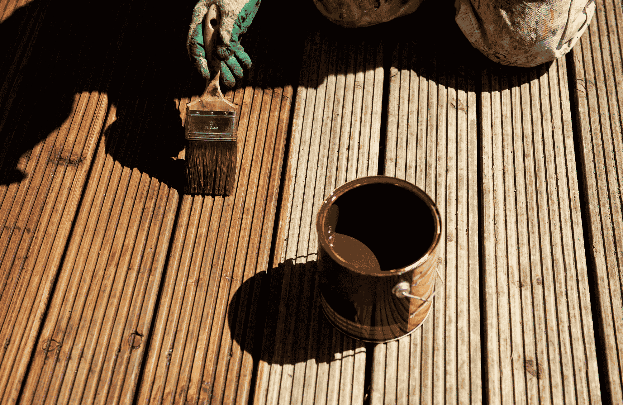 Paintbrush and tin of wood stain on a timber deck