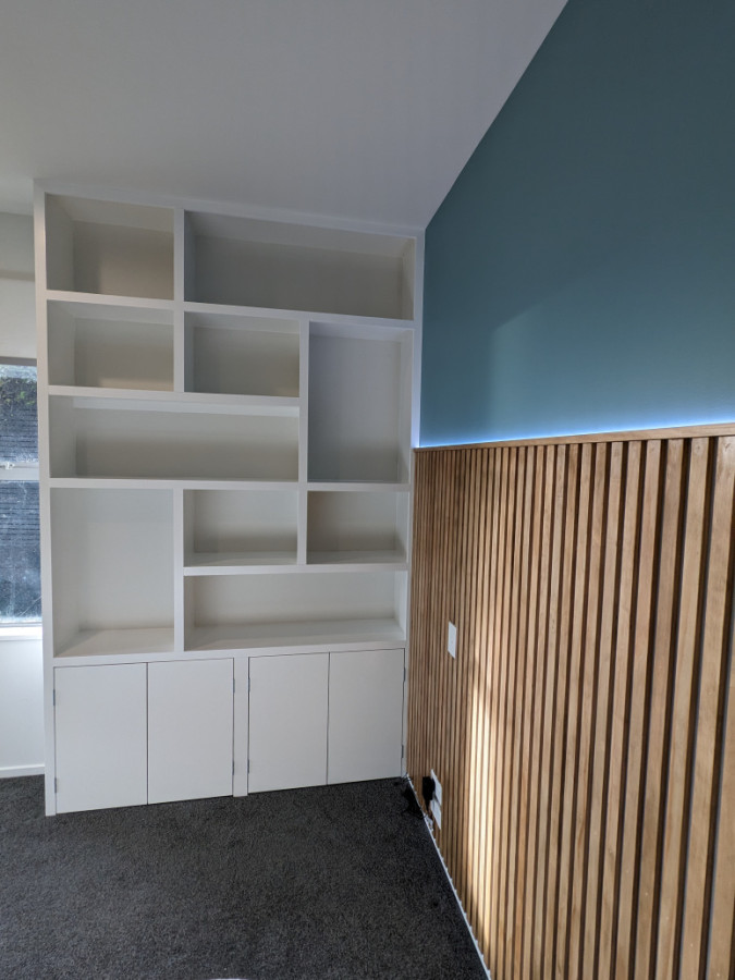 Custom built random shelving and storage cupboards with a decorative wooden bed head