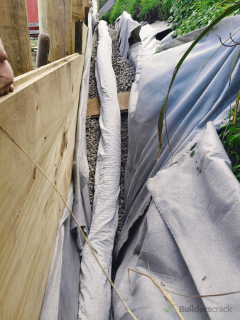 Drainage pipe, wrapped in second layer of cloth, positioned behind the wall on top of porous gravel