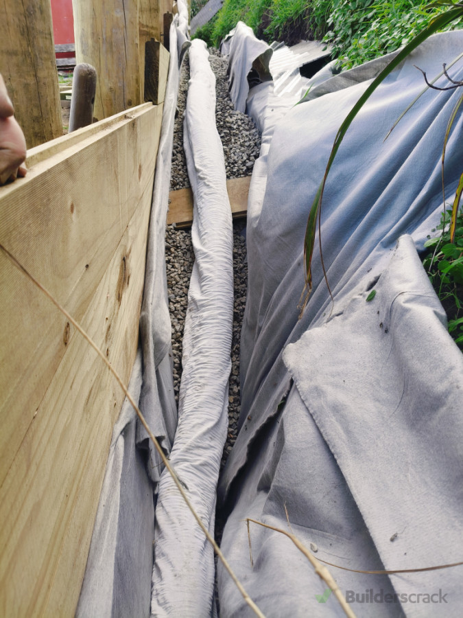 Drainage pipe, wrapped in second layer of cloth, positioned behind the wall on top of porous gravel